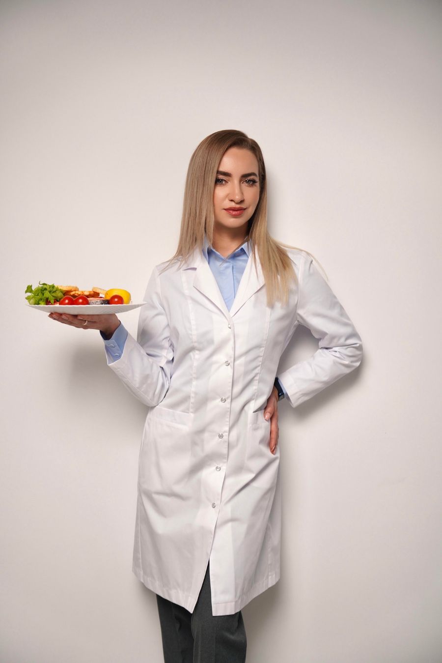 Юлия Калмыкова, нутрициолог, в белом халате с тарелкой овощей